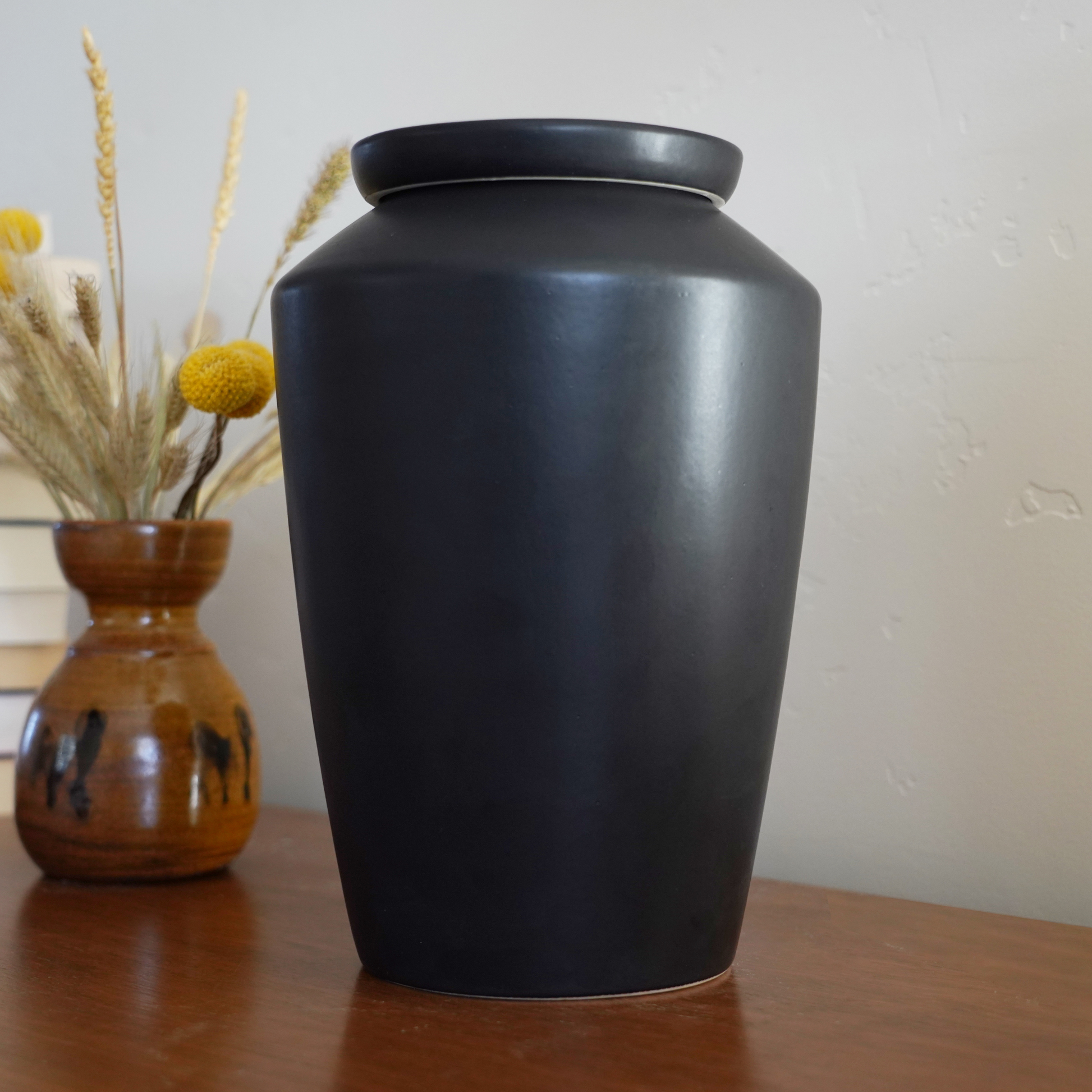 Modern matte black ceramic urn styled as an art piece on a bookshelf, a discreet and beautiful home memorial.