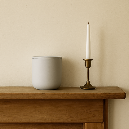 Gray ceramic keepsake urn displayed on a wooden mantel beside a candle in a home memorial setting