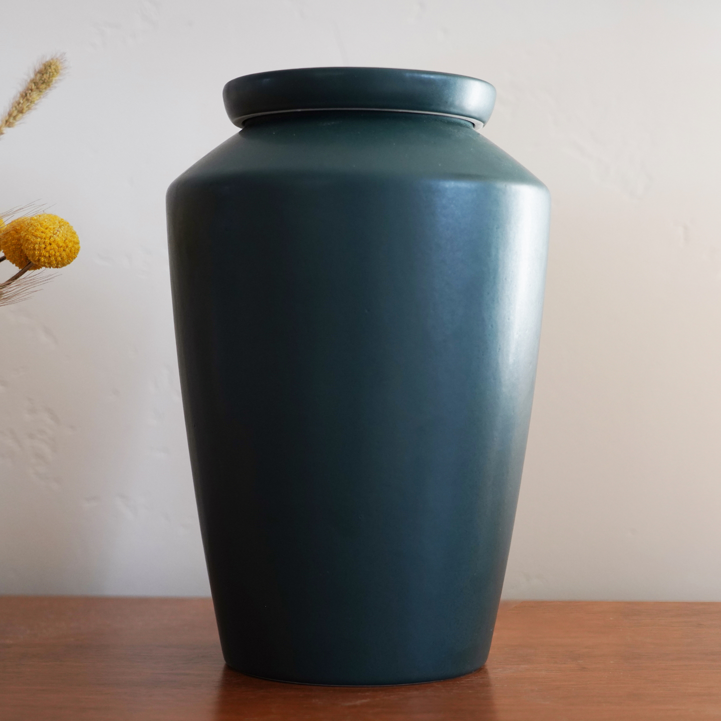 Modern matte green ceramic urn styled as an art piece on a bookshelf, a discreet and beautiful home memorial.