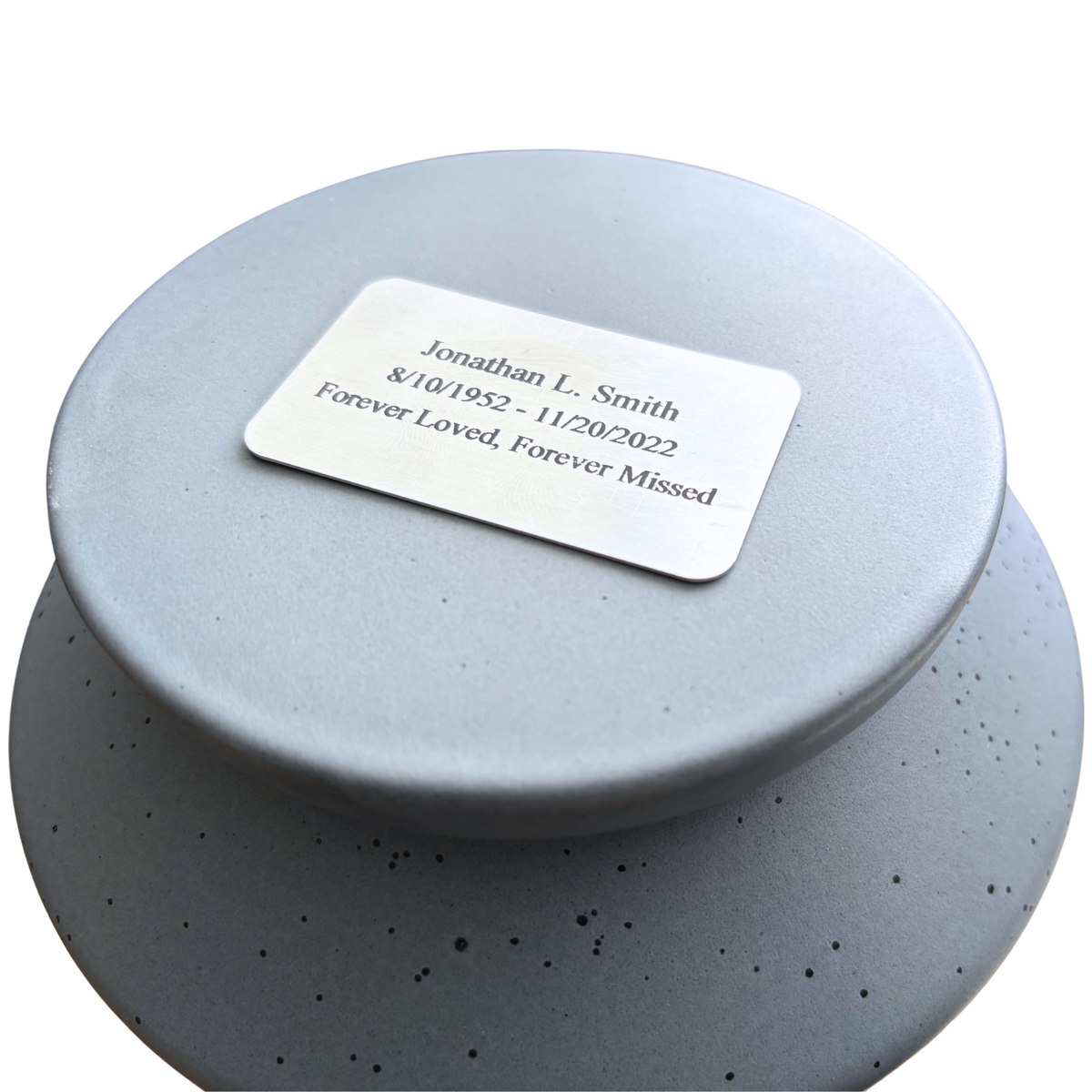 Custom engraved nameplate on the lid of a speckled gray keepsake ceramic urn, personalized memorial for a loved one.