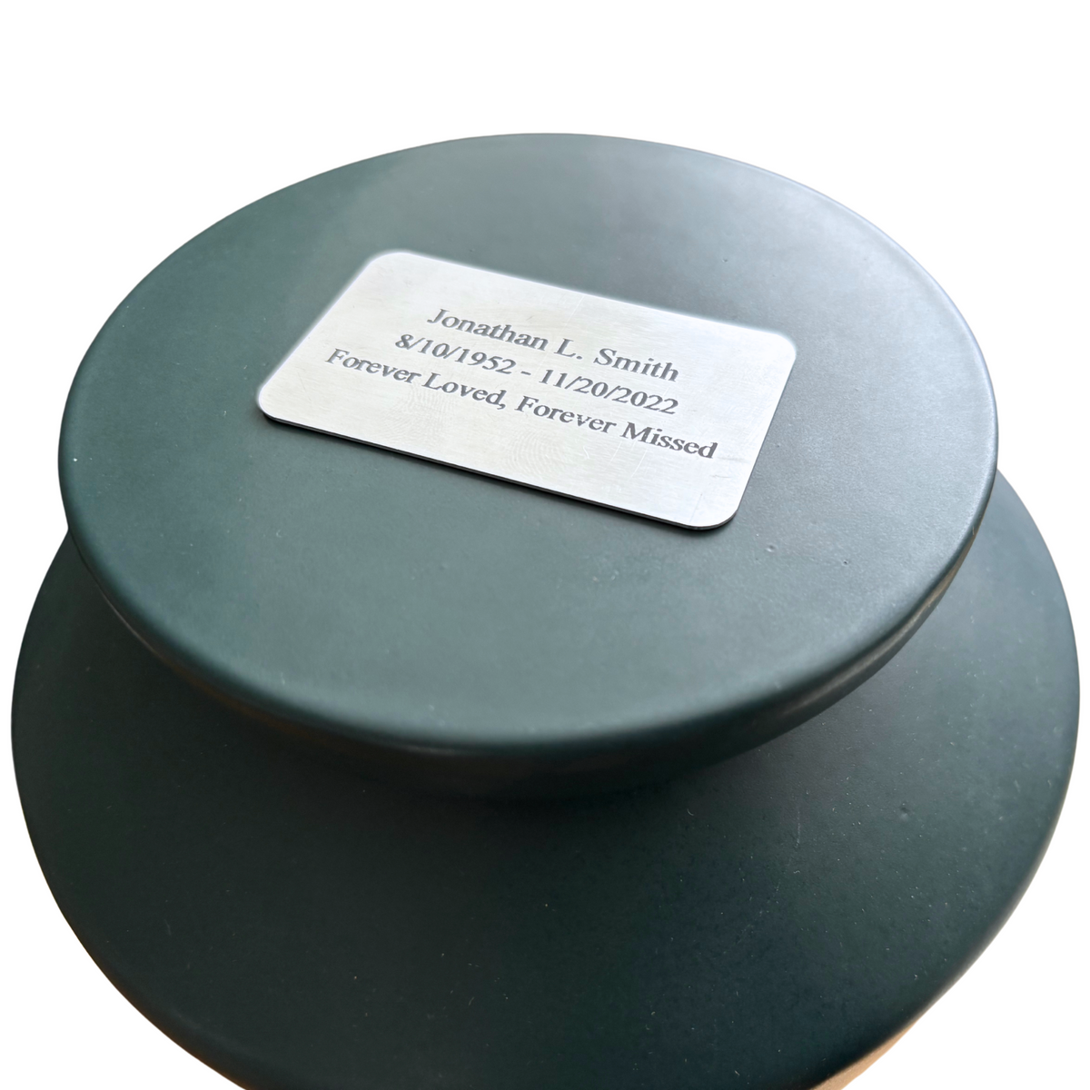 Custom engraved nameplate on the lid of a green keepsake ceramic urn, personalized memorial for a loved one.