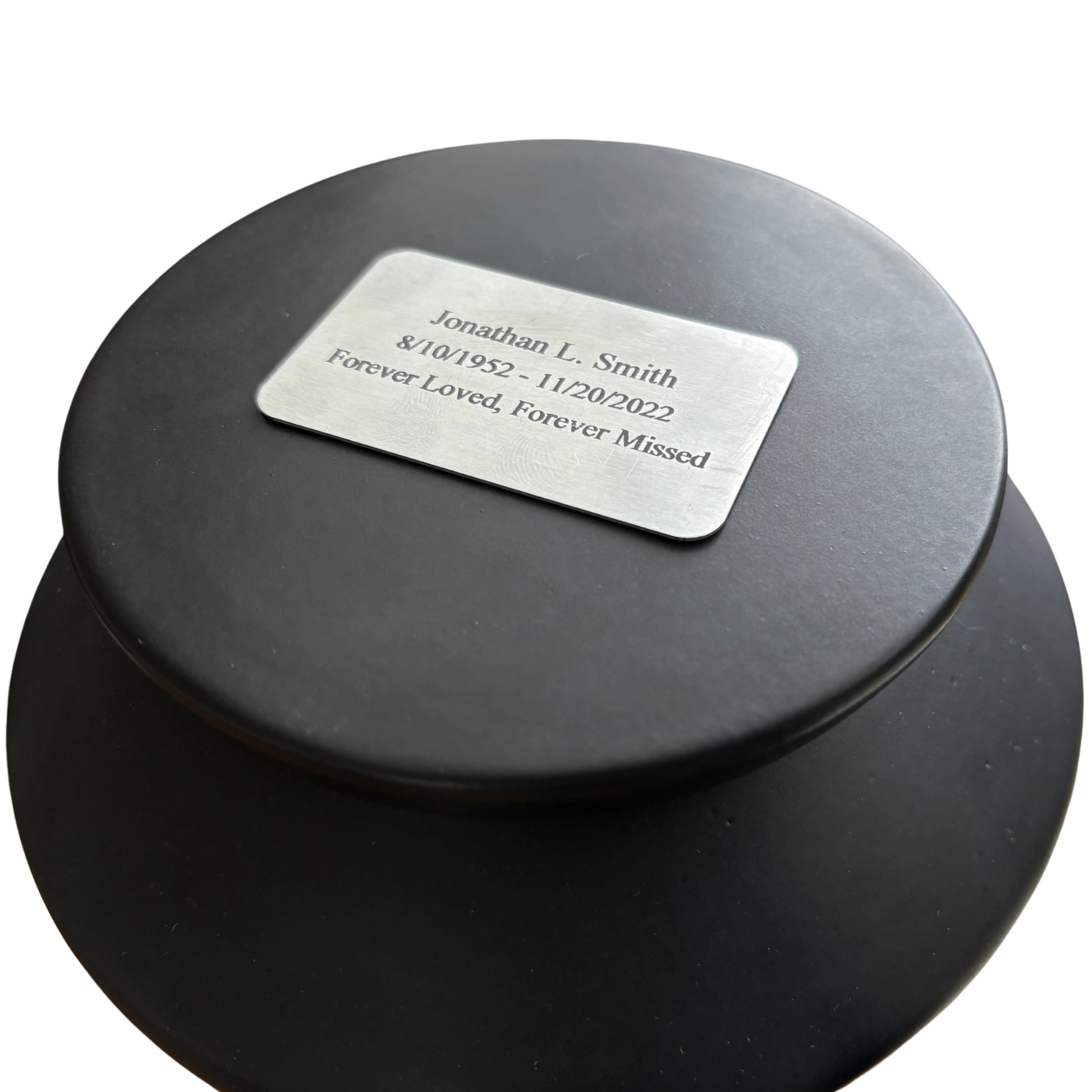 Custom engraved nameplate on the lid of a black ceramic urn, personalized memorial for a loved one.