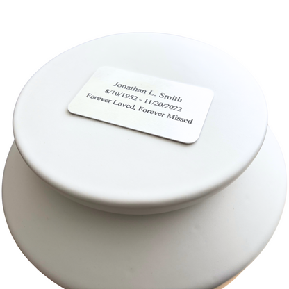 Custom engraved nameplate on the lid of a white ceramic urn, personalized memorial for a loved one.