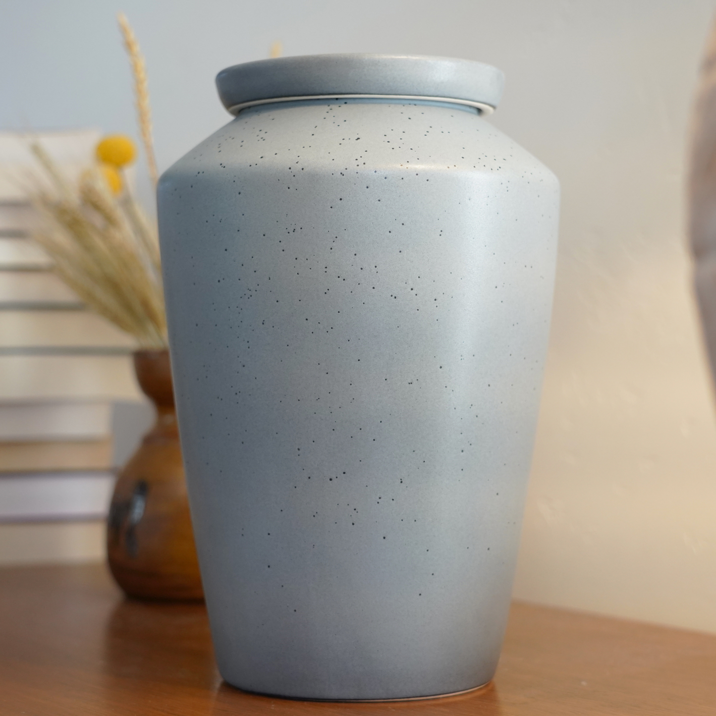 Modern speckled gray ceramic urn styled as an art piece on a bookshelf, a discreet and beautiful home memorial.