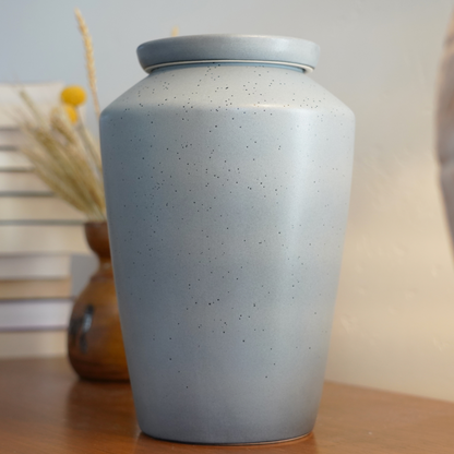 Modern speckled gray ceramic urn styled as an art piece on a bookshelf, a discreet and beautiful home memorial.